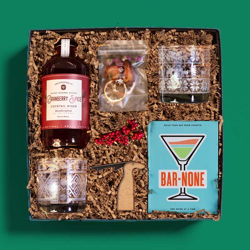 Cheerful holiday gift box with cocktail making ingredients and rocks glasses etched with a sweater pattern